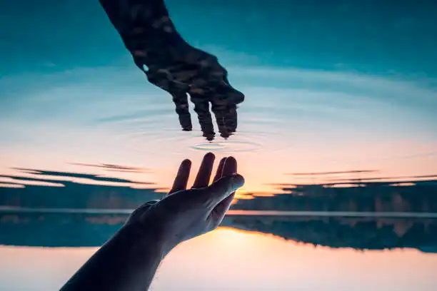 Deux mains qui se rejoignent au-dessus de l'eau d'un lac au coucher du soleil